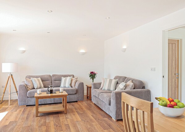 A living room with two sofas, a coffee table, a floor lamp, and a bowl of fruit on a table.