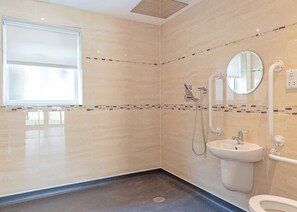 Un baño moderno con ducha, inodoro y lavamanos, que cuenta con un ventanal grande y paredes con azulejos.