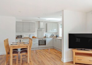 Una cocina moderna con armarios blancos, una mesa de comedor con sillas, un horno, un microondas y un televisor sobre un mueble de madera.