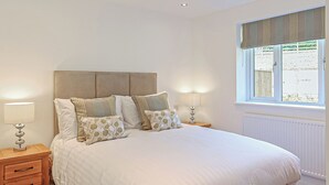 Une chambre à coucher comprenant un lit, deux tables de chevet, une fenêtre avec des rideaux et des spots encastrés au plafond.