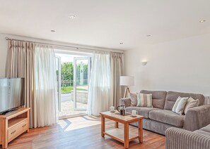 A modern living room with a sofa, a coffee table, a television, and a sliding glass door leading to an outdoor area.