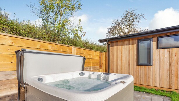 A hot tub in a backyard with a wooden fence and a small wooden building. - Luxurious lodge with vaulted ceilings and a welcoming feature fireplace. (Glastonbury)