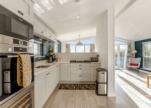 A modern kitchen with white cabinets, a Bosch oven, a coffee machine, and a stainless steel trash bin.