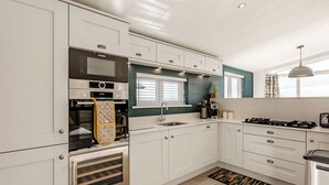 A modern kitchen with white cabinetry, a Bosch oven, a coffee machine, and a gas stove. - Luxurious lodge with vaulted ceilings and a welcoming feature fireplace. (Glastonbury)