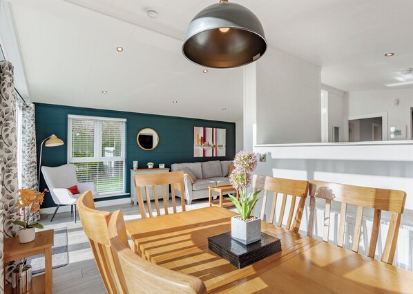 Un comedor con una mesa de madera, sillas y un jarrón central con flores.