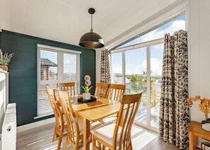 A dining area with a wooden table and chairs, a hanging light fixture, and a view through large windows. - Luxurious lodge with vaulted ceilings and a welcoming feature fireplace. (Glastonbury)
