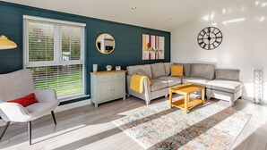 A modern living room with a grey sofa, a white armchair, a wooden coffee table, and a decorative mirror. - Luxurious lodge with vaulted ceilings and a welcoming feature fireplace. (Glastonbury)