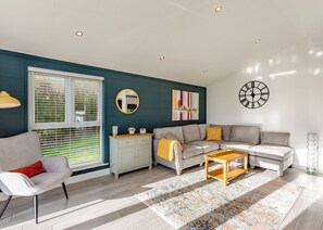 Una sala de estar moderna con un sofá gris, un sillón blanco, una mesa de centro de madera y un espejo decorativo.
