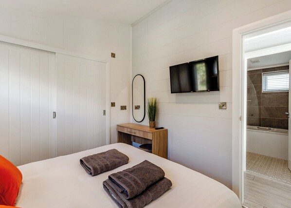A hotel room with a bed, a TV, a mirror, a wooden dresser, and a bathroom with a shower.