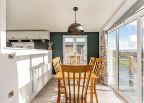 A dining area with a table and chairs, a pendant light, a window with blinds, and a view of the outdoors.