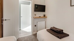 A bedroom with a bed, a TV mounted on the wall, a door leading to another room, and a radiator. - Luxurious lodge with vaulted ceilings and a welcoming feature fireplace. (Glastonbury)