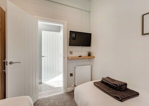 A bedroom with a bed, a TV mounted on the wall, a door leading to another room, and a radiator. - Luxurious lodge with vaulted ceilings and a welcoming feature fireplace. (Glastonbury)