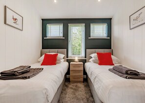 A bedroom with two beds, a nightstand, and a window with blinds. - Luxurious lodge with vaulted ceilings and a welcoming feature fireplace. (Glastonbury)