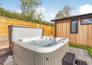 A hot tub in a backyard with a wooden fence and a small wooden building. - Luxurious lodge with vaulted ceilings and a welcoming feature fireplace. (Glastonbury)