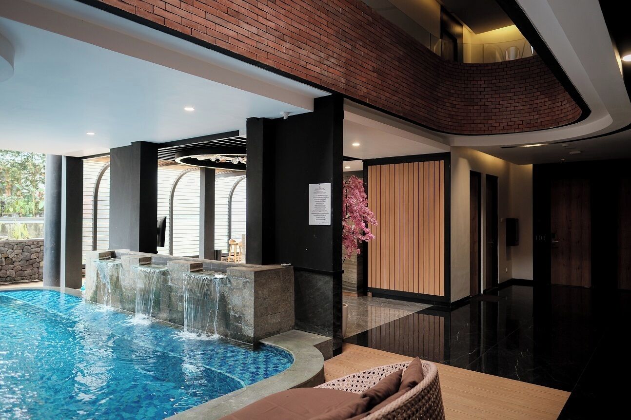 A modern indoor pool area with a waterfall feature, surrounded by wooden paneling and a seating area.