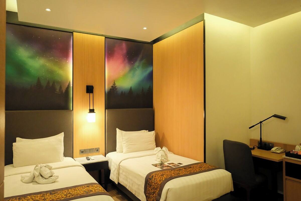 A hotel room with two beds, a desk, and a nightstand. There is a large wall mural of the aurora borealis.