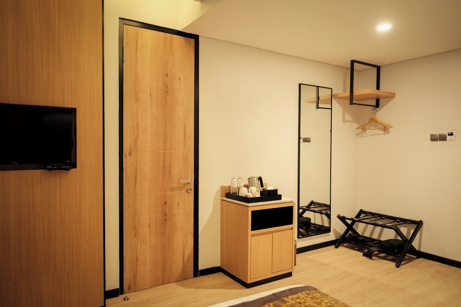 A modern room with a wooden wardrobe, a small cabinet with toiletries, a mirror, and a TV mounted on the wall.