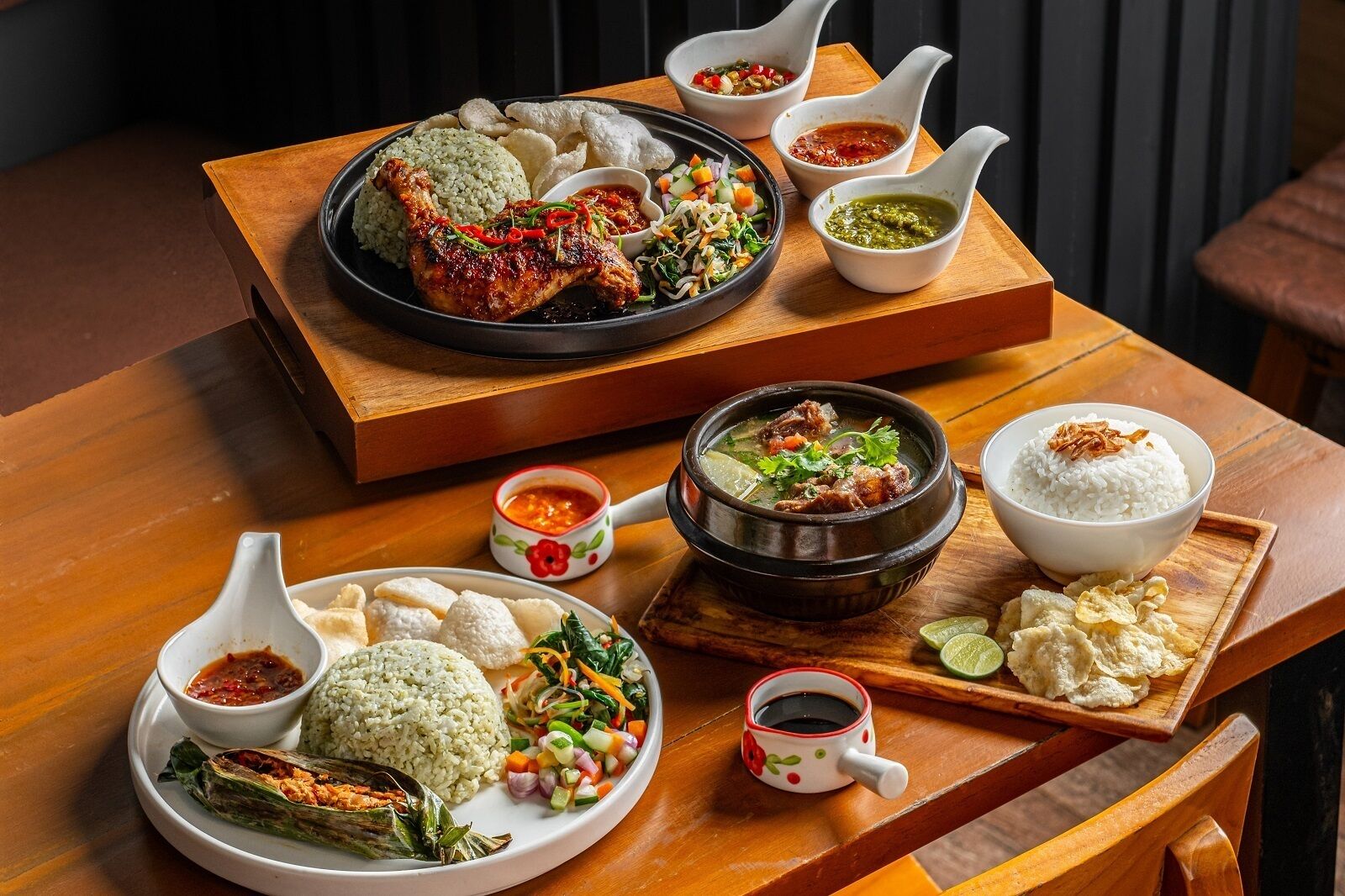 A wooden table with various dishes including rice, grilled chicken, and a soup bowl.