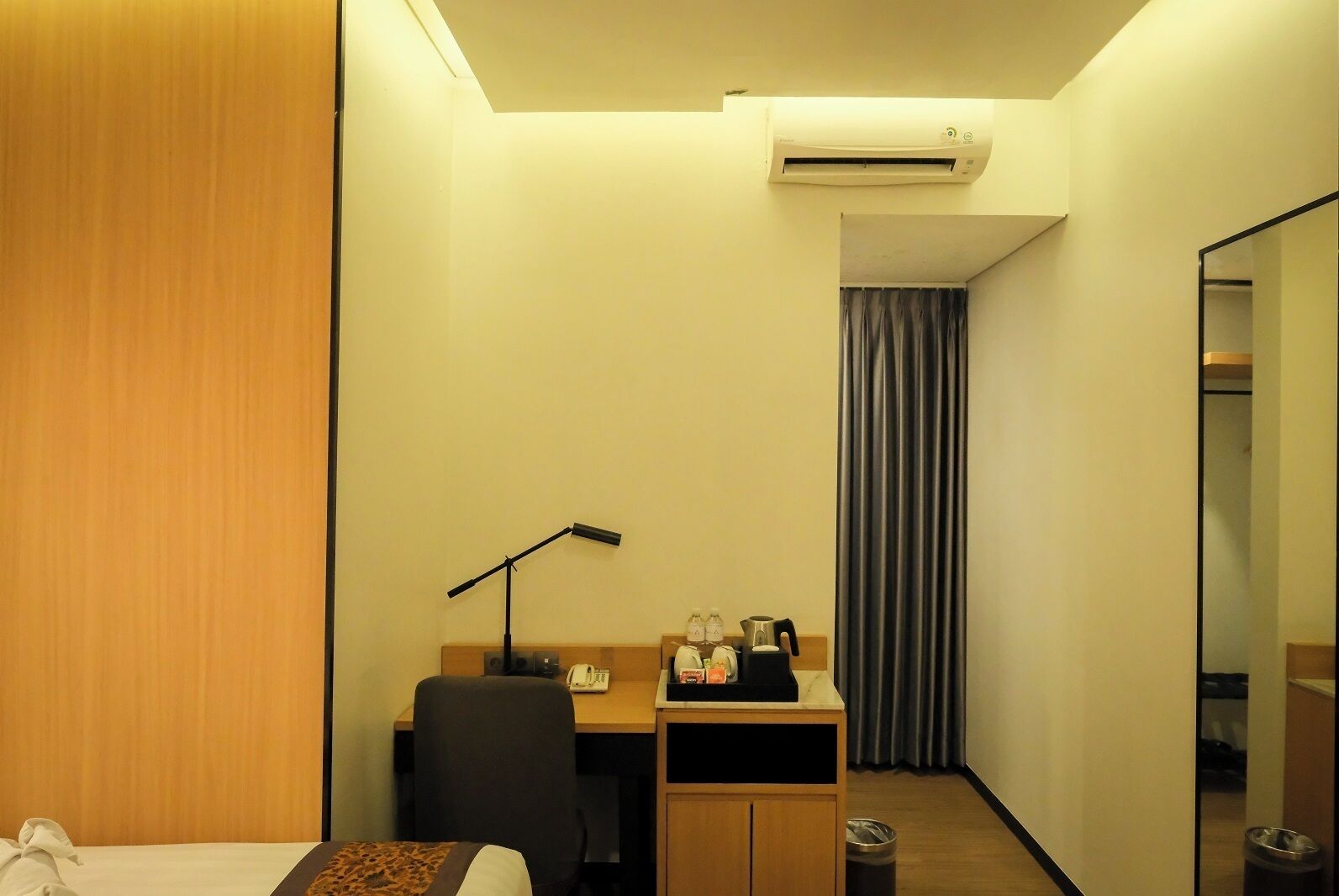 Quarto de hotel com cama, escrivaninha com luminária, cafeteira e lixeira.