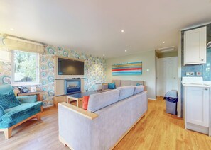 Ein modernes Wohnzimmer mit Sofa, Fernseher, Kamin und Küchenzeile.