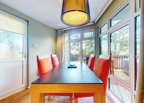 Een kamer met een houten tafel, rode stoelen, grote ramen en uitzicht op het omliggende landschap.