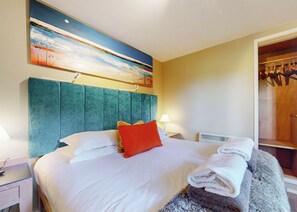 Ein Hotelzimmer mit Bett, einem Bild an der Wand, einem Schrank und einem Nachttisch mit Lampe.