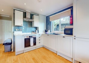 A modern kitchen with white cabinets, a built-in oven, a stainless steel range hood, and a window with a view.
