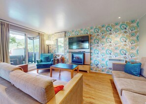 Un salón con sofá, sillón, televisor, chimenea y papel tapiz estampado.