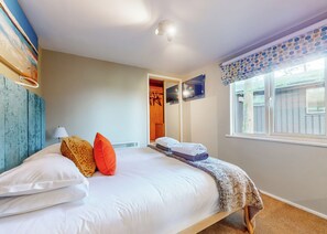 A bedroom with a bed, pillows, a lamp, a TV, a window with curtains, and a door leading to another room.