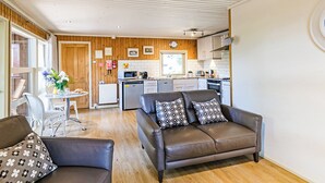 A modern living room with a brown leather sofa, a dining table with chairs, and a kitchen in the background. - Stylish open plan lodge with king-size four poster bed. (Harrogate)