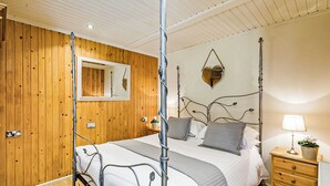 A four-poster bed with a metal frame, a wooden wall with a mirror, and a bedside table with a lamp. - Stylish open plan lodge with king-size four poster bed. (Harrogate)
