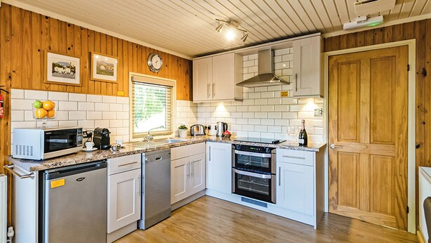 A compact kitchen with white cabinets, a microwave, a dishwasher, a stove, and a wooden ceiling. - Stylish open plan lodge with king-size four poster bed. (Harrogate)