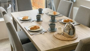 Un tavolo da pranzo apparecchiato con piatti, croissant, tazze e un teiera, circondato da sedie.