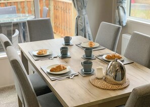 A dining table set with plates, croissants, cups, and a teapot, surrounded by chairs. - 1 bedroom accommodation in Carnforth (Carnforth)