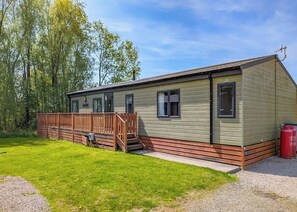 A single-story mobile home with a wooden deck, a small porch, and a gravel driveway. - 1 bedroom accommodation in Carnforth (Carnforth)