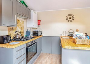 A compact kitchen with a gas stove, toaster, microwave, and a clock on the wall.