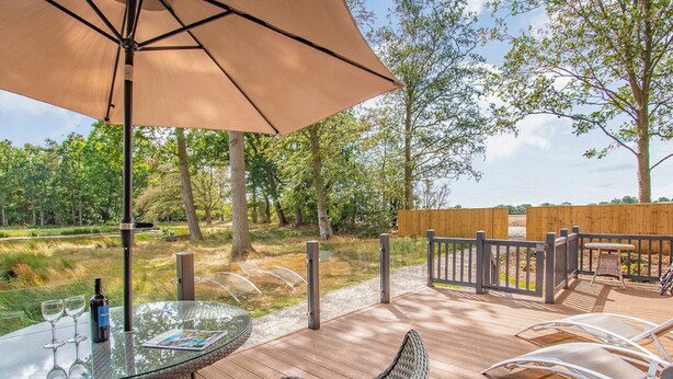 An outdoor deck with wicker furniture, a glass table, and a bottle of wine. - Rowan Boutique Lodge (Aughton)