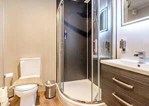 A modern bathroom with a glass-enclosed shower, a toilet, a sink with a mirror, and a trash bin. - Rowan Boutique Lodge (Aughton)