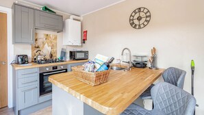 A compact kitchen with a wooden countertop, grey cabinets, a microwave, a kettle, and a clock on the wall. - Rowan Boutique Lodge (Aughton)