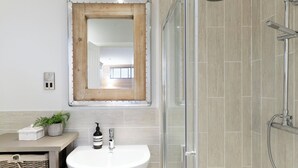 A bathroom with a white sink, a shower with a handheld showerhead, and a mirror with a wooden frame. - 2 bedroom accommodation in Honiton (Honiton)