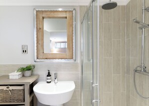 A bathroom with a white sink, a shower with a handheld showerhead, and a mirror with a wooden frame.