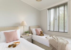 A bedroom with two beds, a nightstand, a lamp, a teddy bear, and a window with blinds.