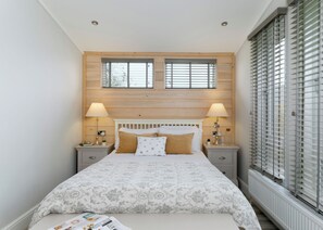 A bedroom with a bed, two bedside tables, two lamps, a window with blinds, and a radiator.