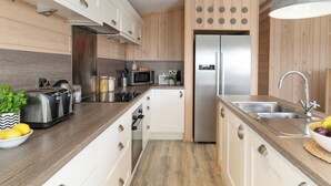 A modern kitchen with white cabinets, a stainless steel refrigerator, a microwave, and a built-in oven. - 2 bedroom accommodation in Honiton (Honiton)