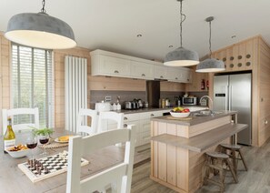 A modern kitchen with wooden cabinets, a central island, stainless steel appliances, and pendant lighting.