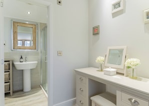 A bathroom with a glass shower enclosure, a white sink, and a vanity with drawers and a mirror.