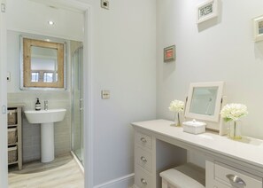 A bathroom with a glass shower enclosure, a white sink, and a vanity with drawers and a mirror.
