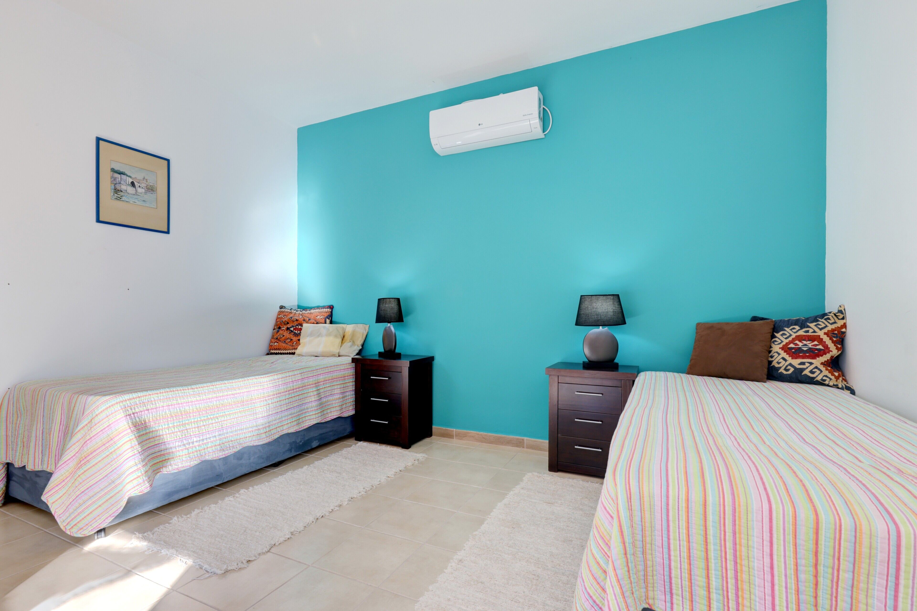 A bedroom with two beds, a white air conditioner, and a framed picture on the wall.