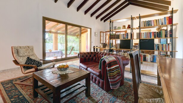 Una sala de estar acogedora con un sofá de cuero, una mesa de centro de madera, una estantería y un ventanal grande.