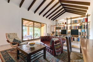 Una sala de estar acogedora con un sofá de cuero, una mesa de centro de madera, una estantería y un ventanal grande.